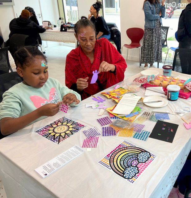 Older Asian woman sitting at an arts and craft table with a young girl at a community centre